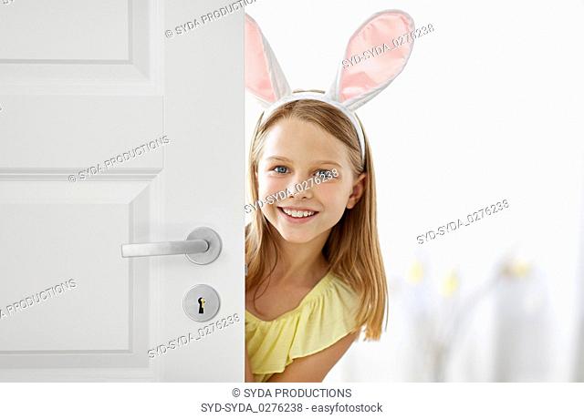 happy girl with easter bunny ears peeking out door