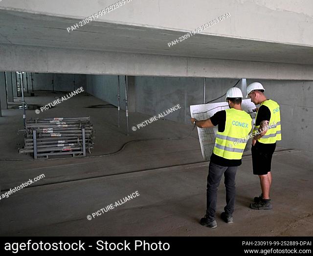 19 September 2023, Berlin: Two construction workers look at a building plan at the construction site of Vonovia's Holzbauquartier project in Berlin Kaulsdorf