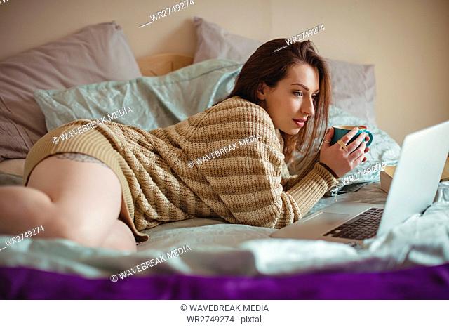 Woman using laptop while having coffee on bed