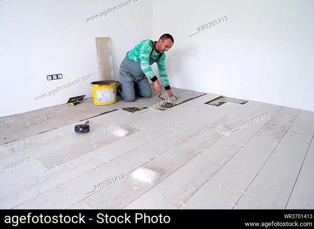 skilled worker installing the ceramic wood effect tiles on the floor Worker making laminate flooring on the construction site of the new apartment
