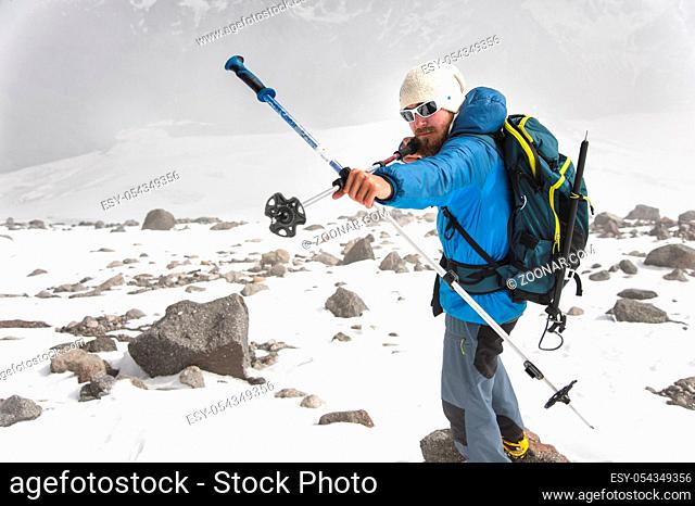 Backpacker in the mountains pretends that he shoots a bow using the example of sticks for Scandinavian walking against the backdrop of an impending storm cloud...