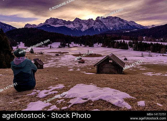 Woman sits at the Geroldsee near Mittenwald / Krün at sunrise and looks into the distance, in the background the Karwendel Mountains, Bavaria, Germany