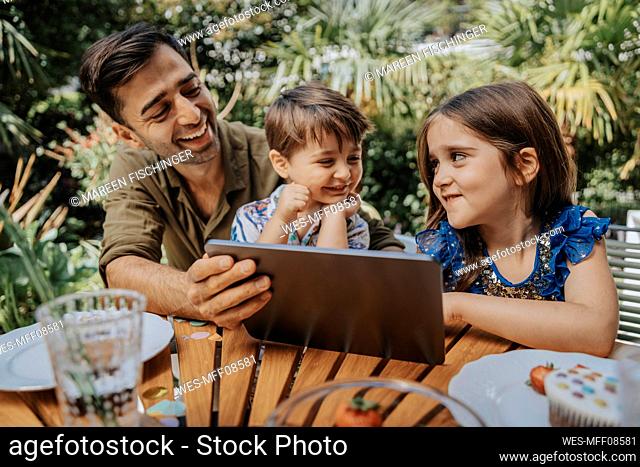 Happy father and children with tablet PC in garden