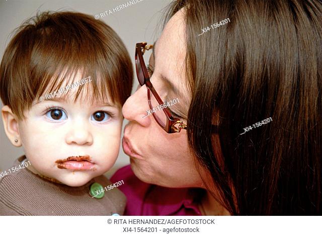 Mommy kissing baby who has lips with lot of chocolate  Baby is looking straight to the camera