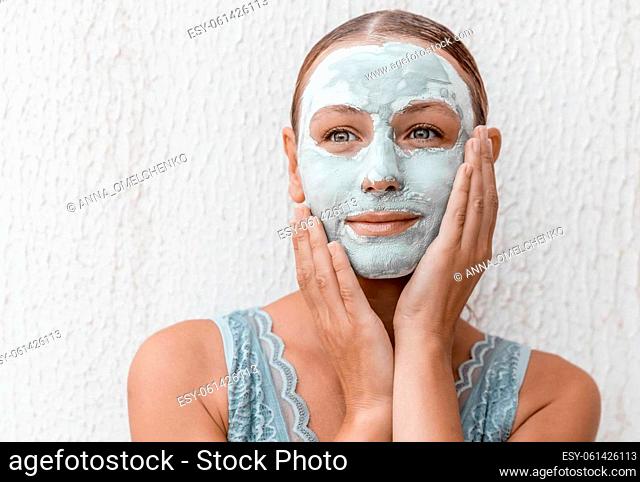 Portrait of a Beautiful Young Woman Applying Clay Mask Isolated on White Background. Enjoying Day Spa in Luxury Beauty Salon