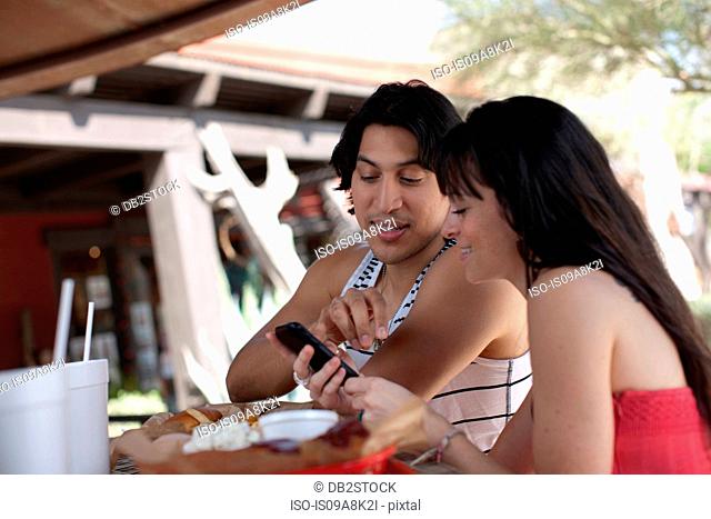Young couple looking at mobile phone in outdoor cafe, smiling