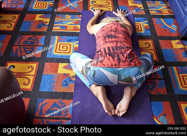 A woman, 60+ years old, in a red top and blue leggings practices yoga in her apartment home, Windsor, Ontario, Canada