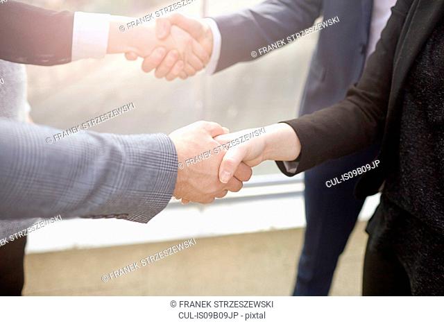 Mid section of businesswomen and businessmen shaking hands