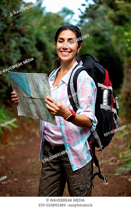 Smiling female hiker looking at map in forest