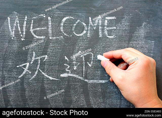 Welcome - word written on a blackboard with a Chinese translation, with a hand holding chalk