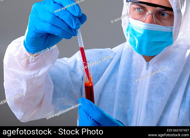 Caucasian male doctor wearing ppe suit holding test-tube