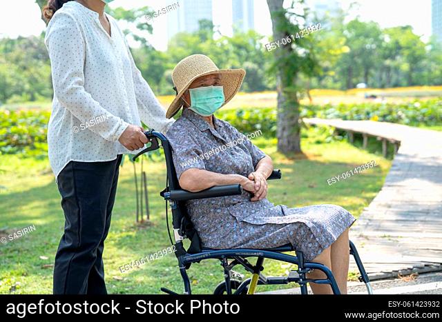 Help Asian senior or elderly old lady woman on wheelchair and wearing a face mask for protect safety infection Covid-19 Coronavirus in park