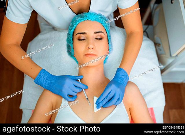 Cosmetician in gloves gives botox injection to female patient on treatment table, top view. Rejuvenation procedure in beautician salon