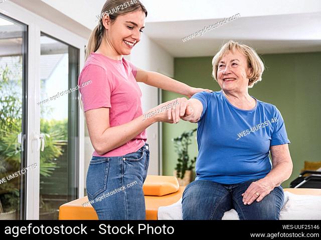 Physical therapist stretching disabled woman's hand at home