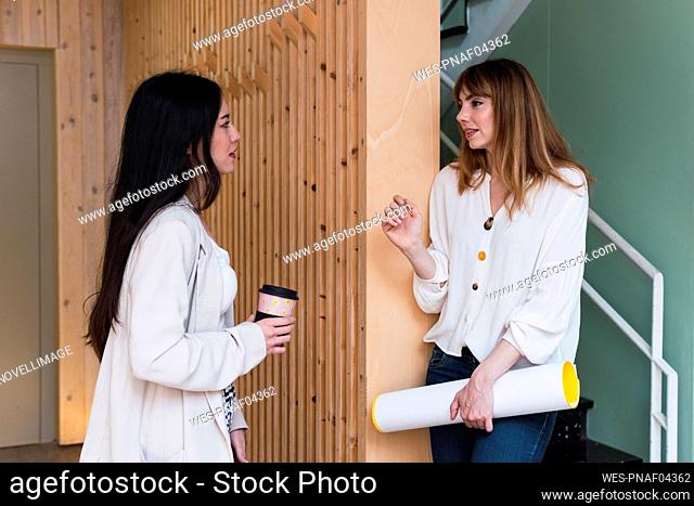 Businesswoman with disposable coffee cup and colleague talking in office