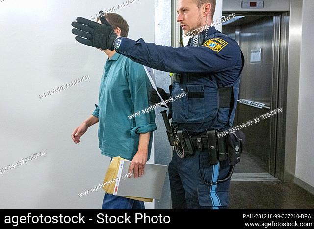 18 December 2023, Bavaria, Regensburg: The defendant walks next to a police officer to the courtroom of the district court