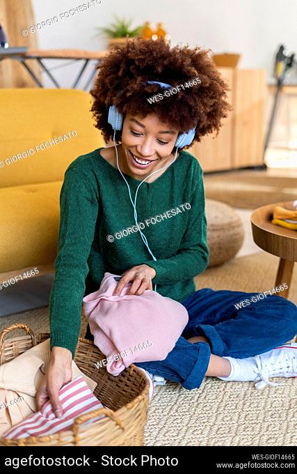 Afro young woman listening music and folding clothes at home