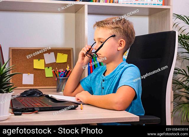 Smart schoolboy with glasses studies at home with laptop and listens attentively to information. Home learning, online education