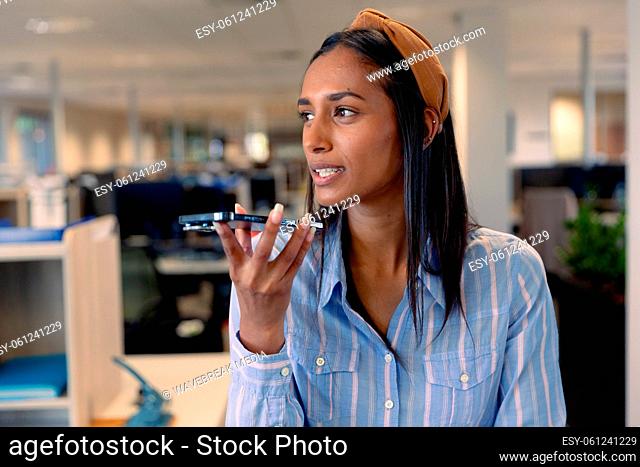 Young african american female advisor talking through smartphone speaker at workplace