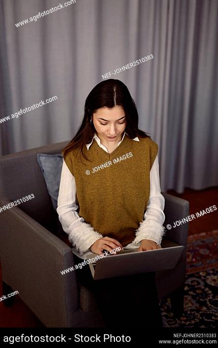 Woman using laptop on armchair