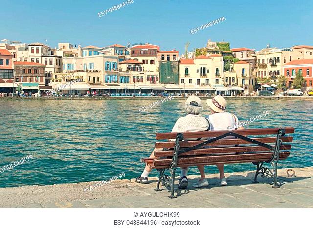 elderly couple resting on bench looking at old part of Chania on sunny summer day, Crete, Greece
