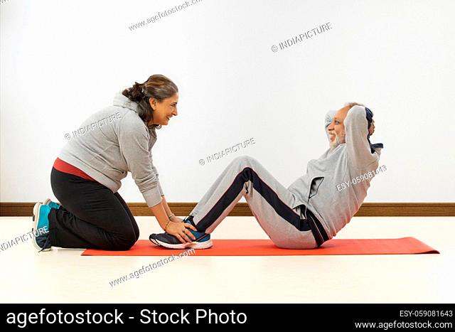 A SENIOR ADULT WOMAN HAPPILY HELPING HUSBAND TO DO EXERCISE