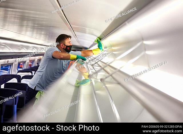 05 June 2020, North Rhine-Westphalia, Dortmund: An employee of DB-Fernverkehrswerk Dortmund cleans luggage racks in an ICE with face masks and rubber gloves