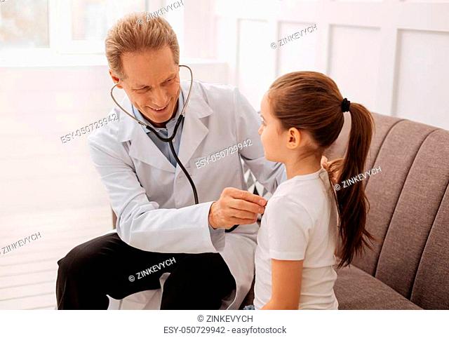 Take a deep breath. Handsome trained joyful doctor hearing to his little patient breathing while making some tests before writing out some medication