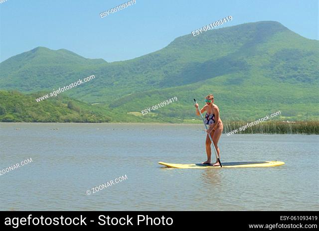 Young woman practicing Stand Up Paddle on lake, yellow board, paddling. Paddleboarding