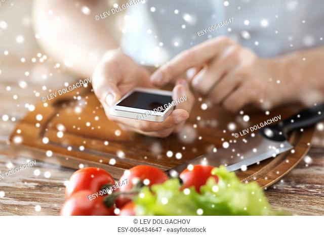 cooking, people, technology and home concept - closeup of man reading recipe from smartphone and vegetables on table in kitchen