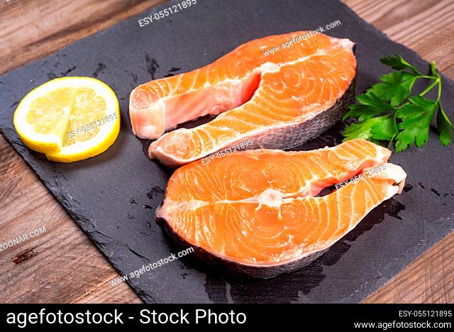 Two fresh raw salmon steaks with lemon and parsley on the rustic table