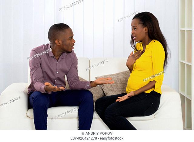 Young Couple Sitting On Sofa Quarreling With Each Other