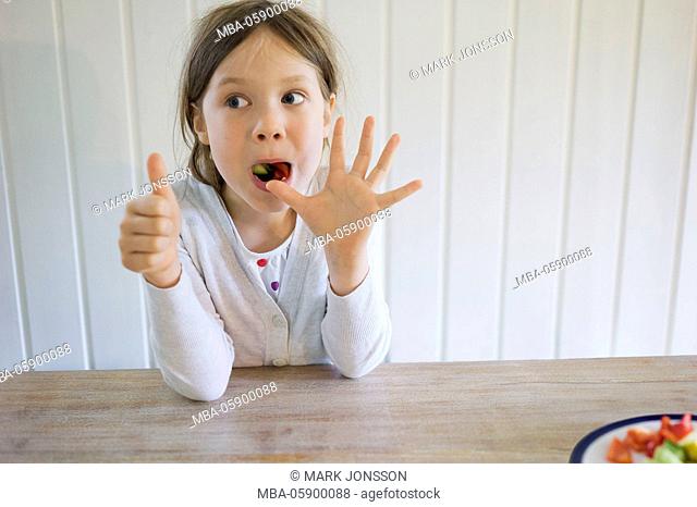 Girl sits at the table and stuffs several pieces of peppers and zucchini in her mouth