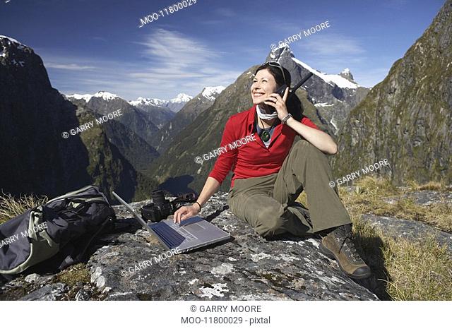 Woman using walkie-talkie and laptop on mountain peak
