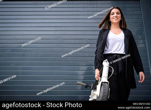 Businesswoman holding electric push scooter in front of shutter