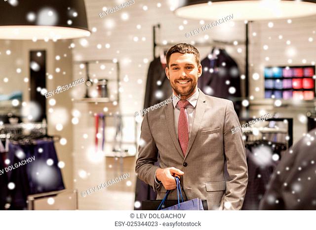 sale, fashion, retail, business style and people concept - happy man with shopping bags at clothing store over snow