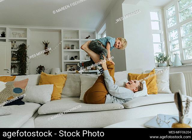 Mother picking son on leg while playing on sofa at home