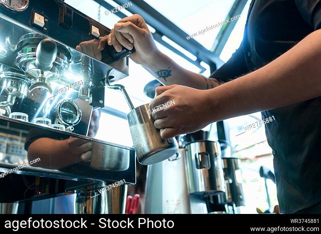 High angle view close-up of the hand of a barista holding a stainless mug while using a modern coffee machine