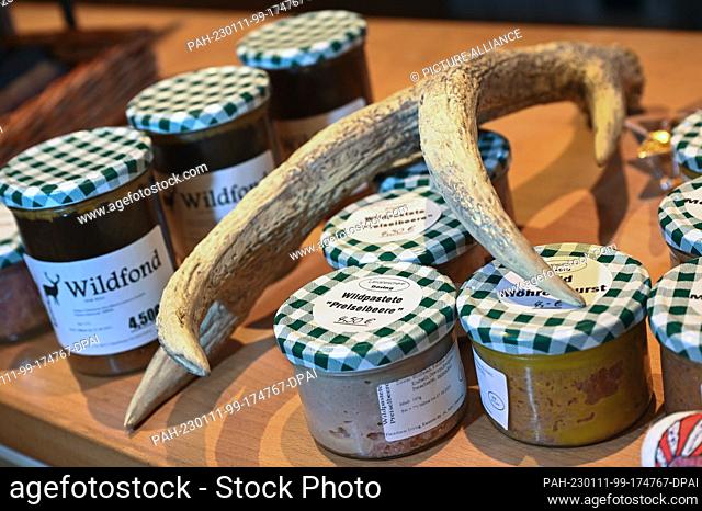 PRODUCTION - 06 January 2023, Hessen, Kassel: Game stock and game pté in jars lie next to antlers in the game store. The meat of venison, deer