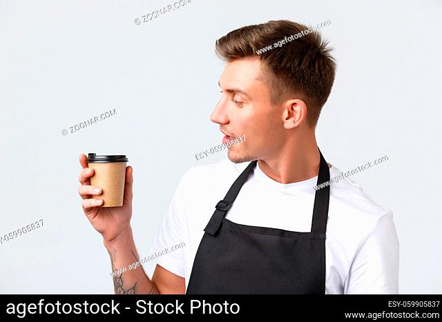 Cafe and restaurants, coffee shop owners and retail concept. Close-up of friendly good-looking barista looking at paper cup with cappuccino, handing over order