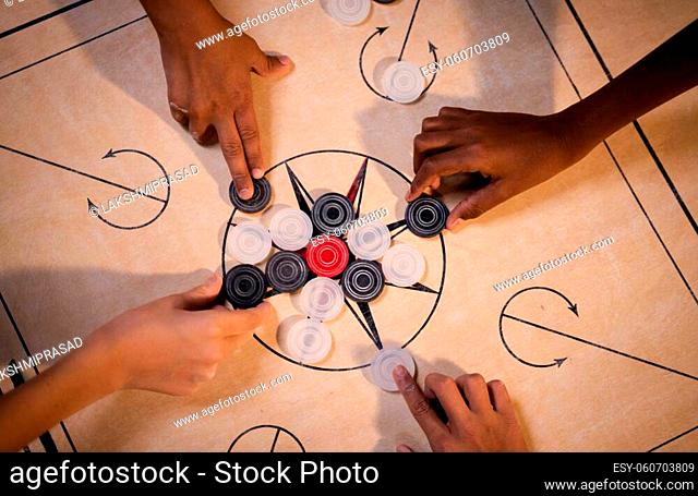 Top view of multiethnic Kids hands arranging carrom board game coins for playing match - Concept of leisure activities, teamwork, cooperation