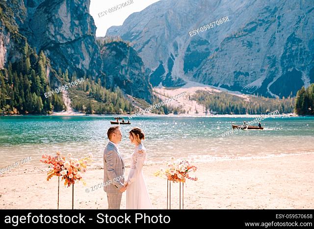The groom dons a bride's ring, in place for the ceremony, with an arch of autumn floral columns, against the backdrop of Lago di Braies in Italy