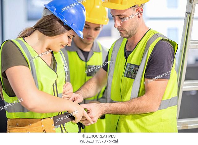 Construction worker helping colleague with tool belt