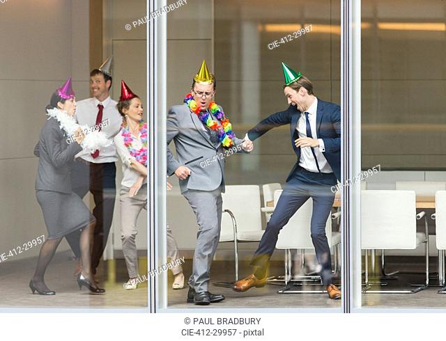 Playful business people in party hats dancing at conference room window