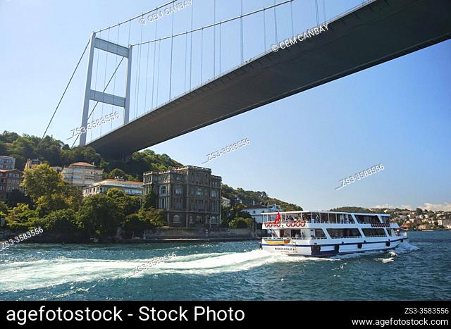 Touristic cruise boat in front of the Rumelihisari (also known as Rumelian Castle and Roumeli Hissar Castle) village under the Bosphorus bridge at the European...