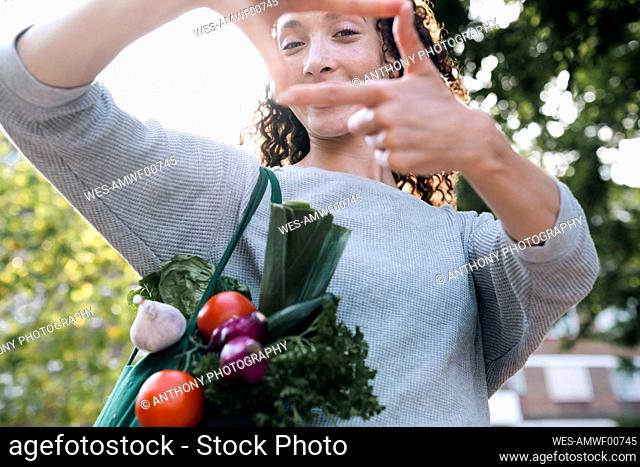 Woman with bag of vegetables looking through finger frame
