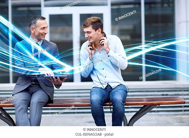 Businessman and young man watching digital tablet and waves of blue light