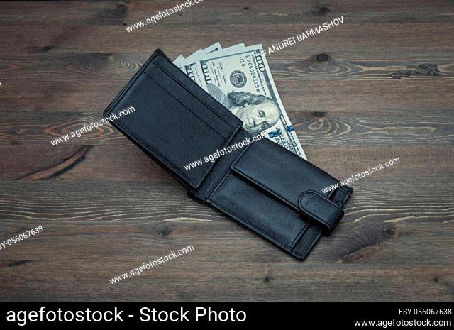 Opened black purse with bills of one hundred dollars on a table