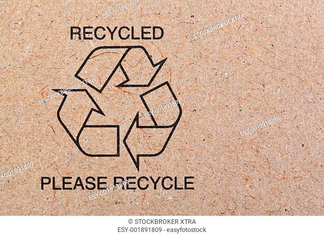 Close up photo of the recycle symbol printed on a recycled cardboard background