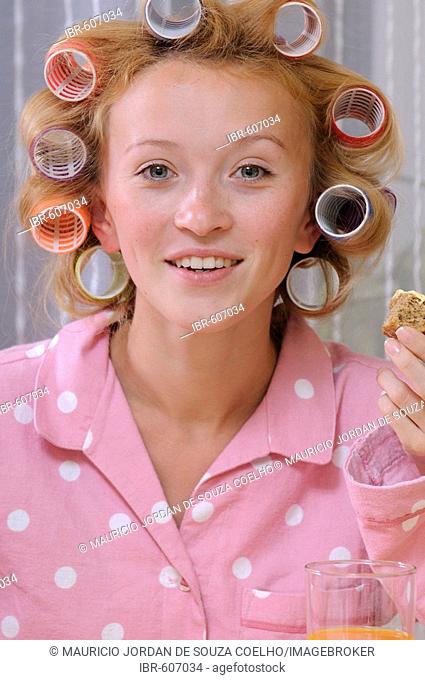 Redheaded woman wearing pajamas with curlers in her hair eating breakfast